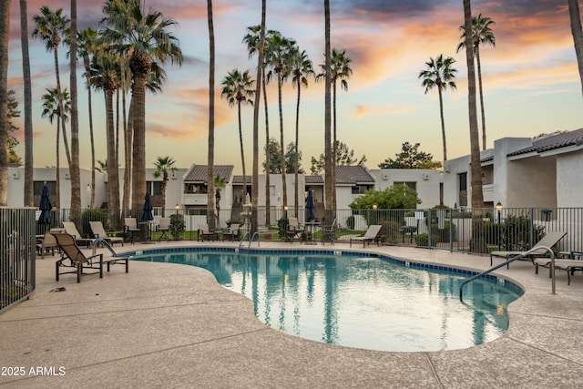 pool at dusk with a patio area, a community pool, fence, and a residential view