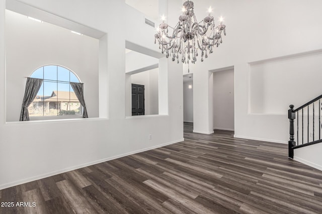 unfurnished living room with dark wood-type flooring, an inviting chandelier, and a high ceiling