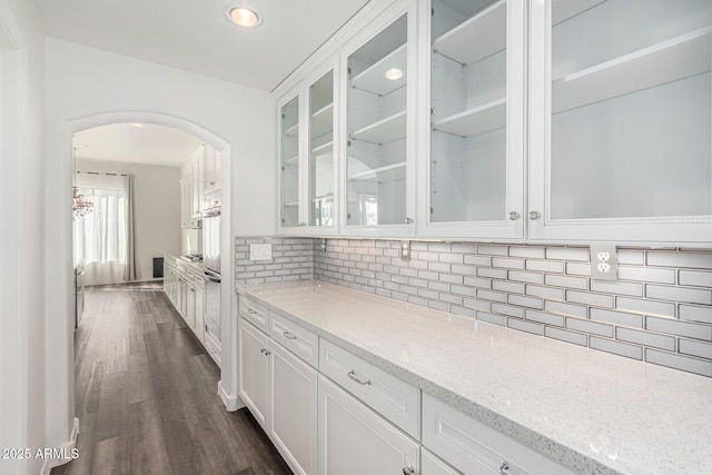 bar featuring dark wood-type flooring, light stone counters, stainless steel oven, decorative backsplash, and white cabinets