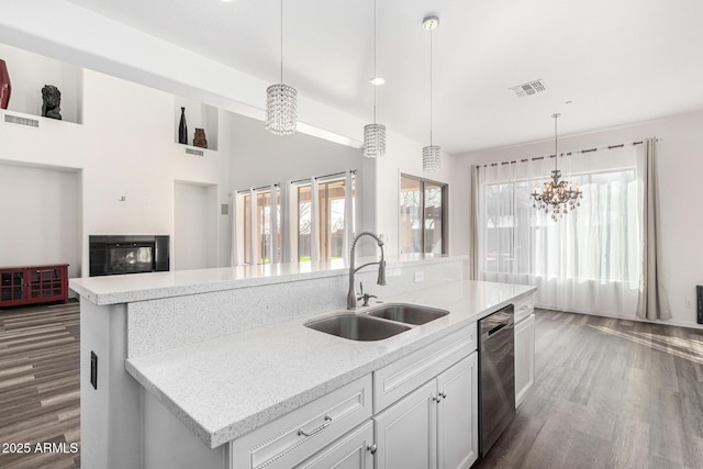 kitchen featuring sink, light stone counters, decorative light fixtures, stainless steel dishwasher, and a kitchen island with sink