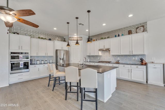 22927 E Via Del Oro, Queen Creek, AZ 85142 - kitchen with stainless steel appliances, dark countertops, tasteful backsplash, white cabinetry, and an island with sink