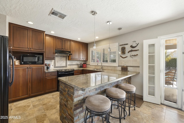 kitchen featuring under cabinet range hood, a peninsula, a sink, visible vents, and black appliances