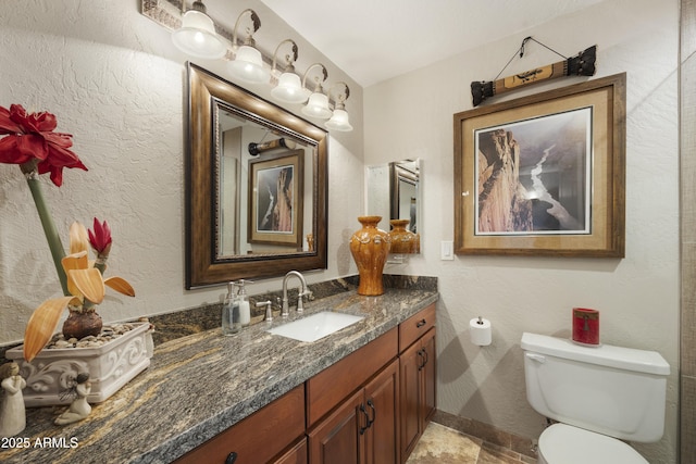 bathroom featuring a textured wall, vanity, and toilet