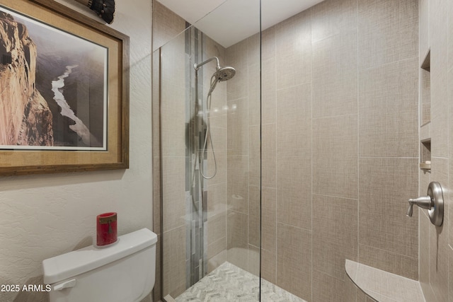 bathroom featuring tiled shower, a textured wall, and toilet