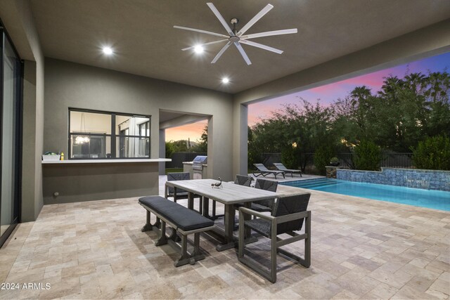 pool at dusk with ceiling fan and a patio