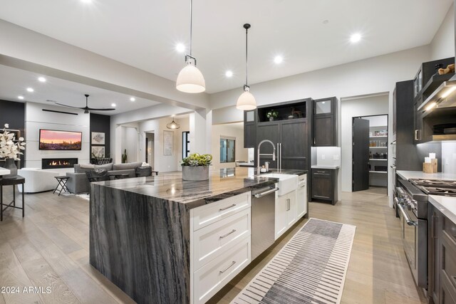 kitchen with sink, white cabinetry, hanging light fixtures, appliances with stainless steel finishes, and an island with sink