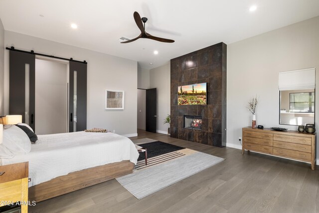 bedroom with dark hardwood / wood-style floors, a fireplace, a barn door, and ceiling fan