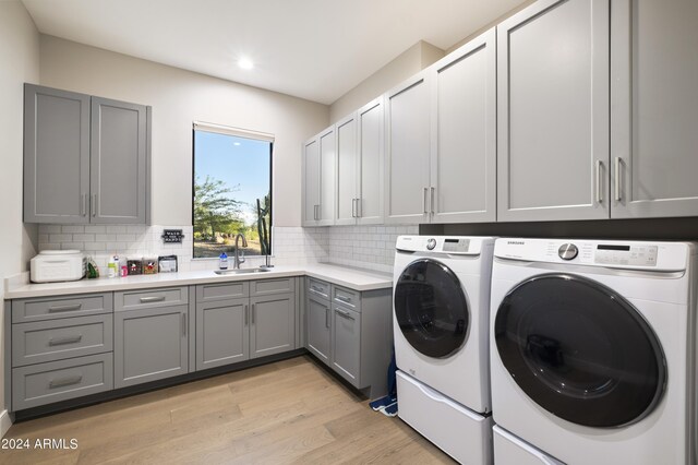 washroom featuring washer and dryer, sink, cabinets, and light wood-type flooring