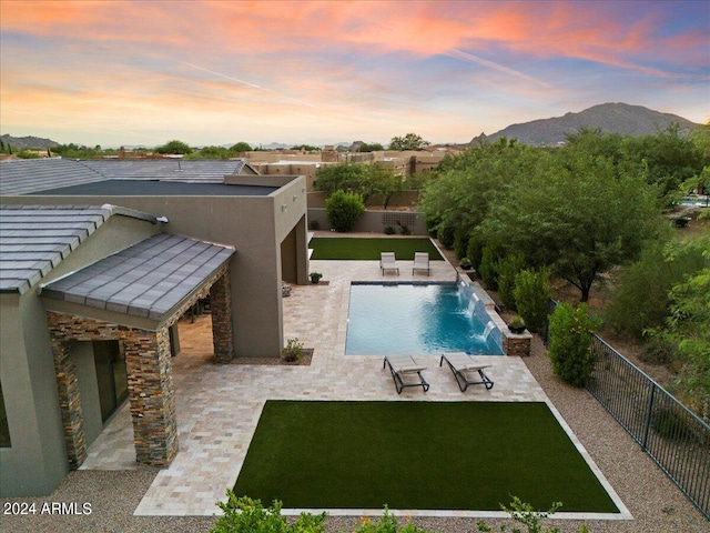 pool at dusk featuring pool water feature, a yard, and a mountain view