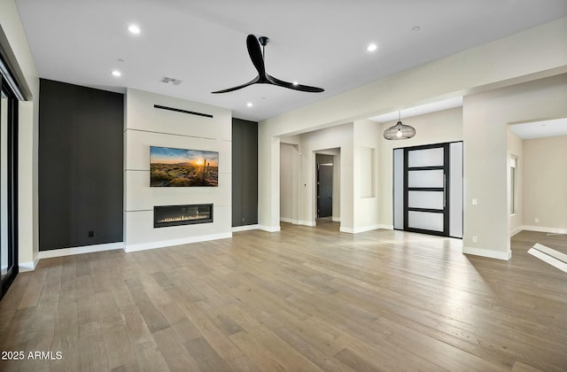 unfurnished living room featuring ceiling fan, a fireplace, and light hardwood / wood-style floors