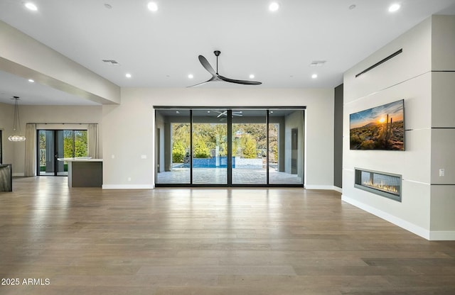 unfurnished living room with ceiling fan, wood-type flooring, and a wealth of natural light