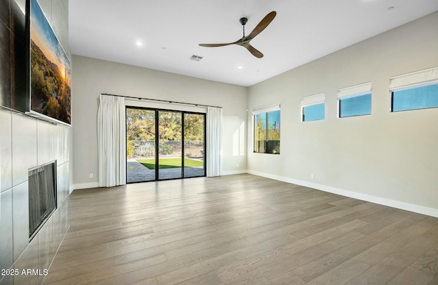 unfurnished living room featuring ceiling fan, wood-type flooring, and a tiled fireplace