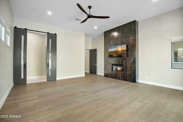 unfurnished living room featuring a tile fireplace, a barn door, ceiling fan, and light wood-type flooring