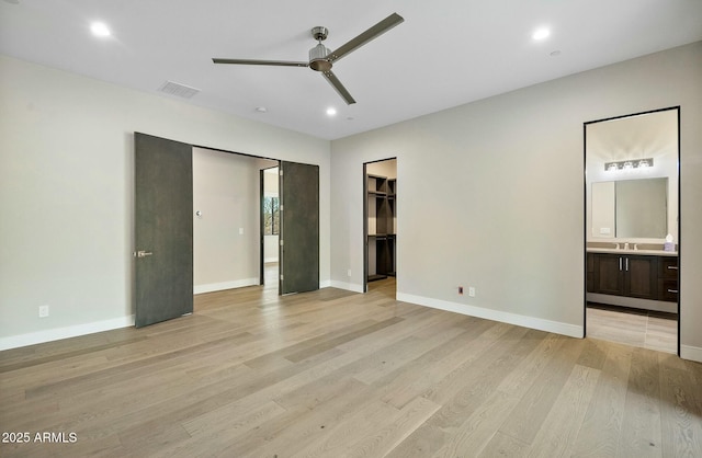 unfurnished bedroom with connected bathroom, a spacious closet, light hardwood / wood-style flooring, and ceiling fan