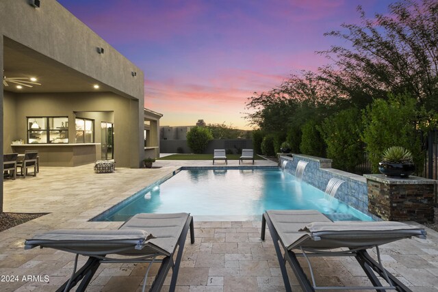 pool at dusk featuring pool water feature and a patio area