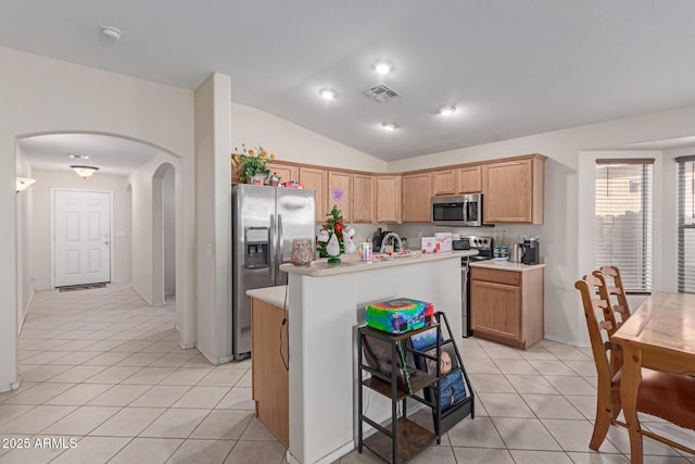 kitchen featuring lofted ceiling, light tile patterned floors, sink, stainless steel appliances, and an island with sink