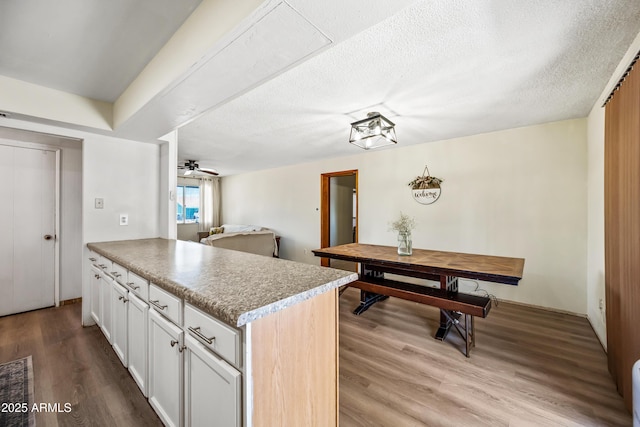 kitchen featuring wood finished floors, white cabinetry, a peninsula, ceiling fan, and a textured ceiling