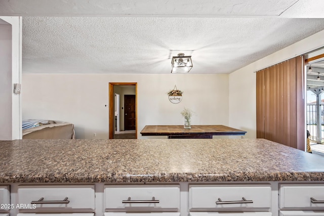 kitchen featuring dark countertops, white cabinets, and a textured ceiling