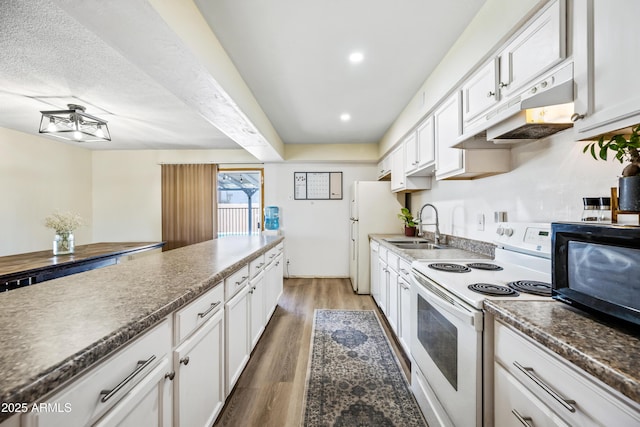 kitchen featuring white appliances, under cabinet range hood, a sink, light wood finished floors, and dark countertops