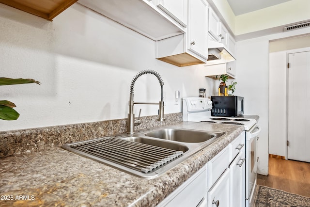 kitchen featuring white electric range, a sink, white cabinets, wood finished floors, and light countertops