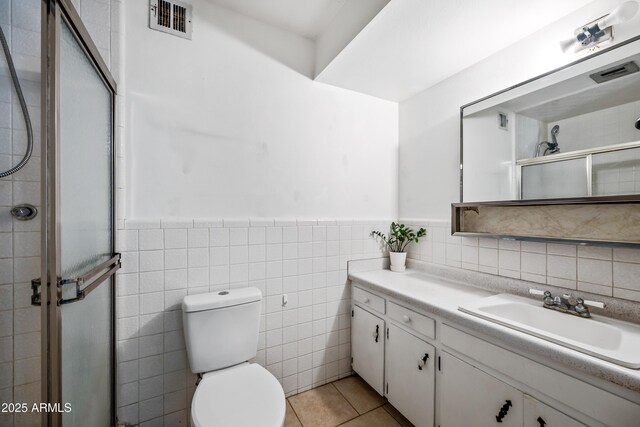 full bathroom featuring a stall shower, vanity, toilet, tile patterned flooring, and a wainscoted wall