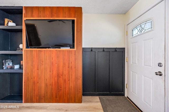 entryway with a textured ceiling, wainscoting, wood finished floors, and wooden walls
