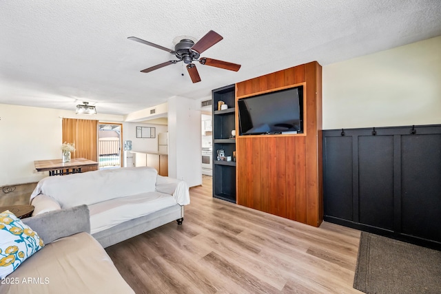 living room with ceiling fan, a textured ceiling, and light wood finished floors