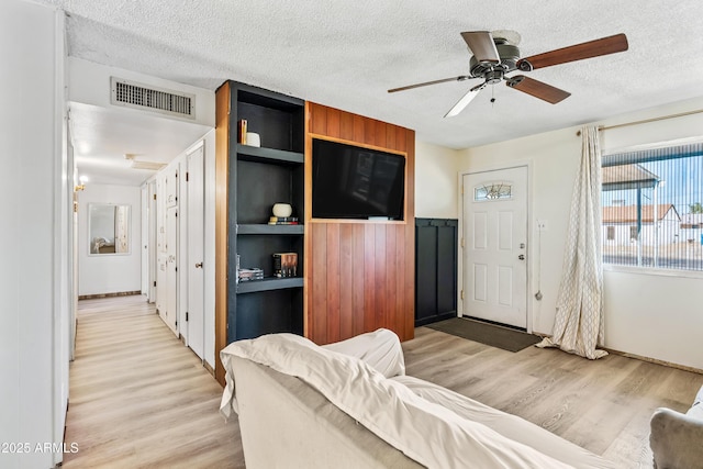 living room with a textured ceiling, light wood-style flooring, and ceiling fan