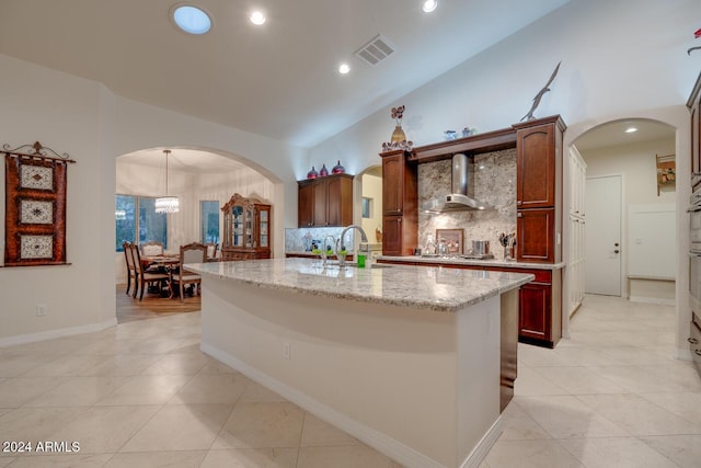 kitchen with tasteful backsplash, wall chimney exhaust hood, vaulted ceiling, sink, and a center island with sink