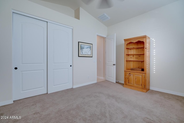 unfurnished bedroom featuring light colored carpet, vaulted ceiling, a closet, and ceiling fan