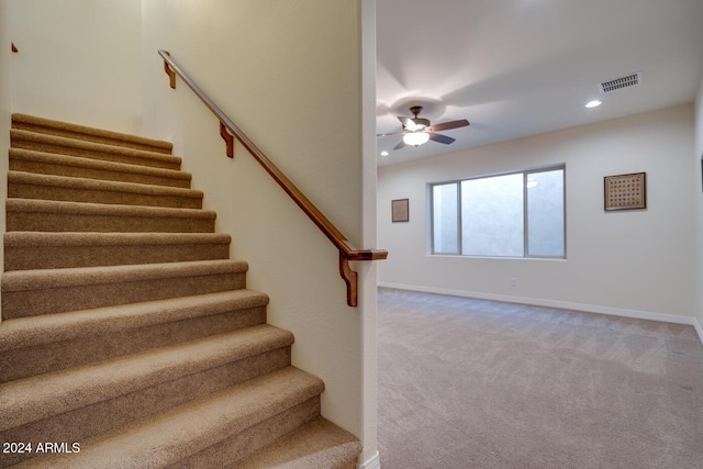 stairs featuring ceiling fan and carpet