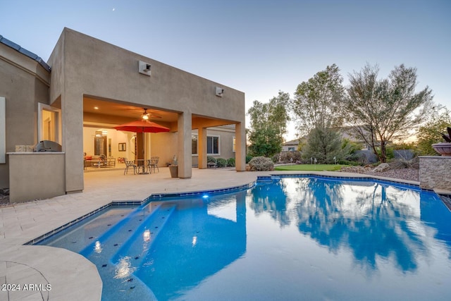 pool at dusk featuring ceiling fan, area for grilling, and a patio area