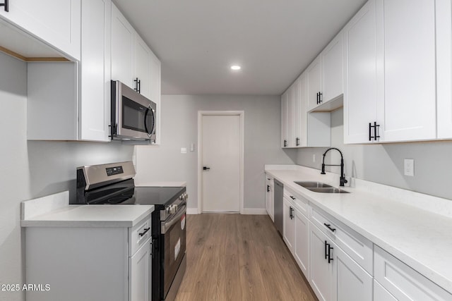 kitchen featuring appliances with stainless steel finishes, white cabinets, a sink, and light wood-style flooring