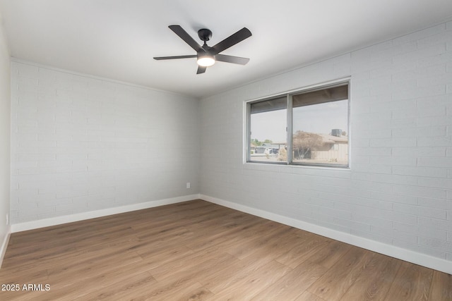 empty room with a ceiling fan, brick wall, baseboards, and light wood finished floors