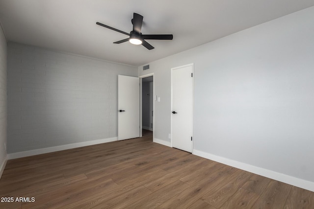 unfurnished bedroom featuring baseboards, visible vents, brick wall, ceiling fan, and wood finished floors