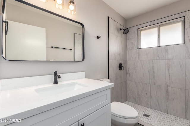 full bathroom featuring a tile shower, vanity, and toilet