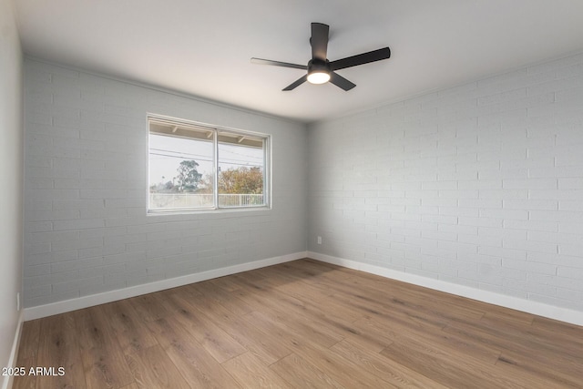 spare room with brick wall, baseboards, ceiling fan, and wood finished floors