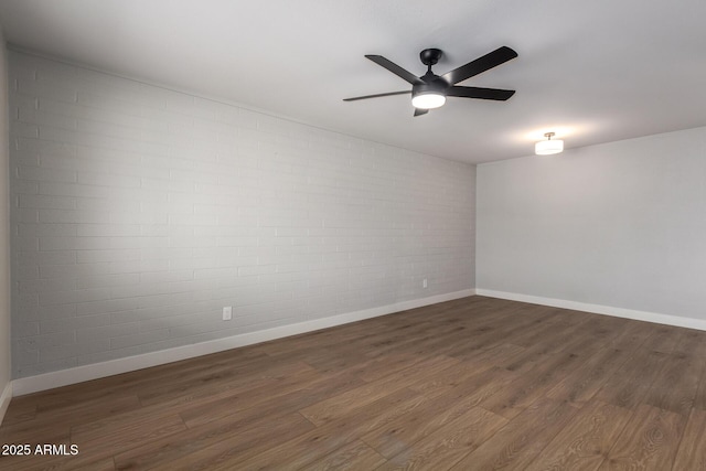 empty room featuring ceiling fan, brick wall, wood finished floors, and baseboards