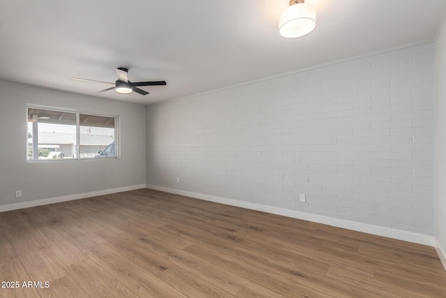 empty room with a ceiling fan, brick wall, baseboards, and wood finished floors