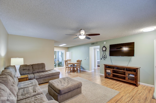 living room featuring ceiling fan, a textured ceiling, and light wood-type flooring