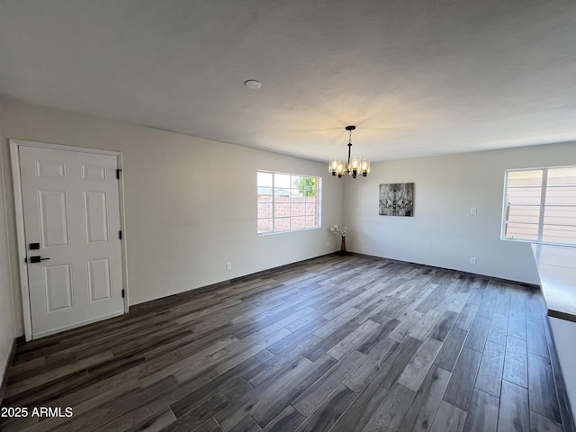 spare room featuring dark wood-type flooring and a chandelier