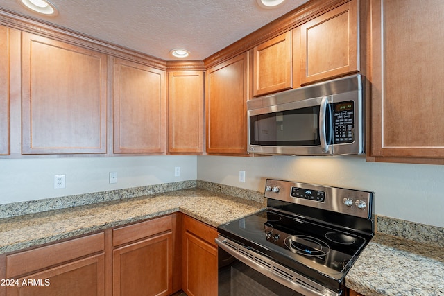 kitchen featuring light stone counters, a textured ceiling, and appliances with stainless steel finishes