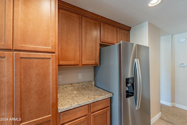 kitchen featuring light stone countertops, stainless steel refrigerator with ice dispenser, and a textured ceiling