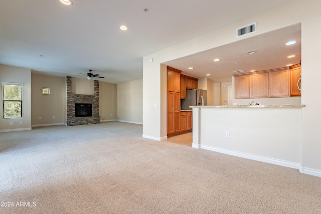 unfurnished living room featuring a fireplace, light carpet, and ceiling fan