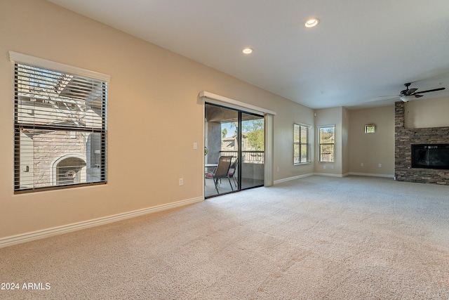 unfurnished living room featuring ceiling fan, a fireplace, and light colored carpet