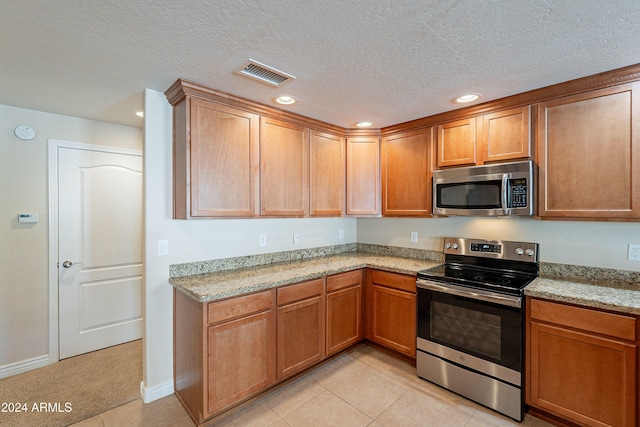 kitchen with light tile patterned floors, light stone countertops, a textured ceiling, and appliances with stainless steel finishes