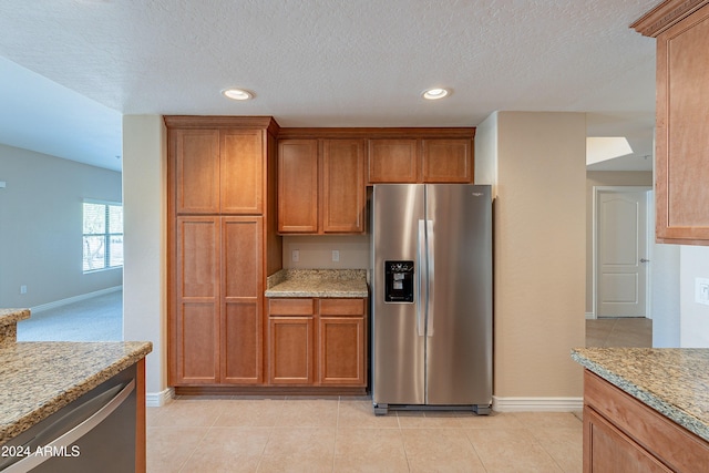 kitchen featuring stainless steel fridge with ice dispenser, light tile patterned floors, a textured ceiling, and light stone counters