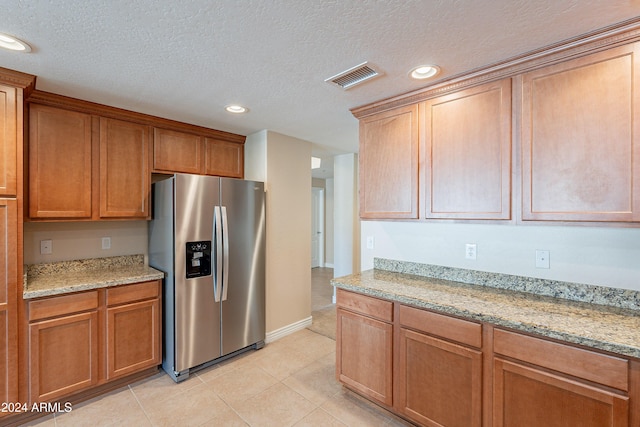 kitchen with light stone counters, stainless steel fridge with ice dispenser, a textured ceiling, and light tile patterned floors