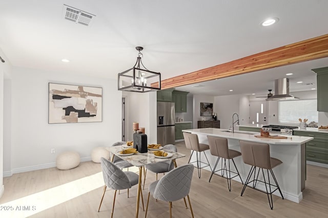 dining area with ceiling fan with notable chandelier, beam ceiling, light wood-type flooring, and sink