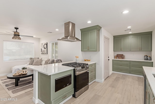 kitchen featuring appliances with stainless steel finishes, wall chimney exhaust hood, ceiling fan, light hardwood / wood-style flooring, and green cabinetry